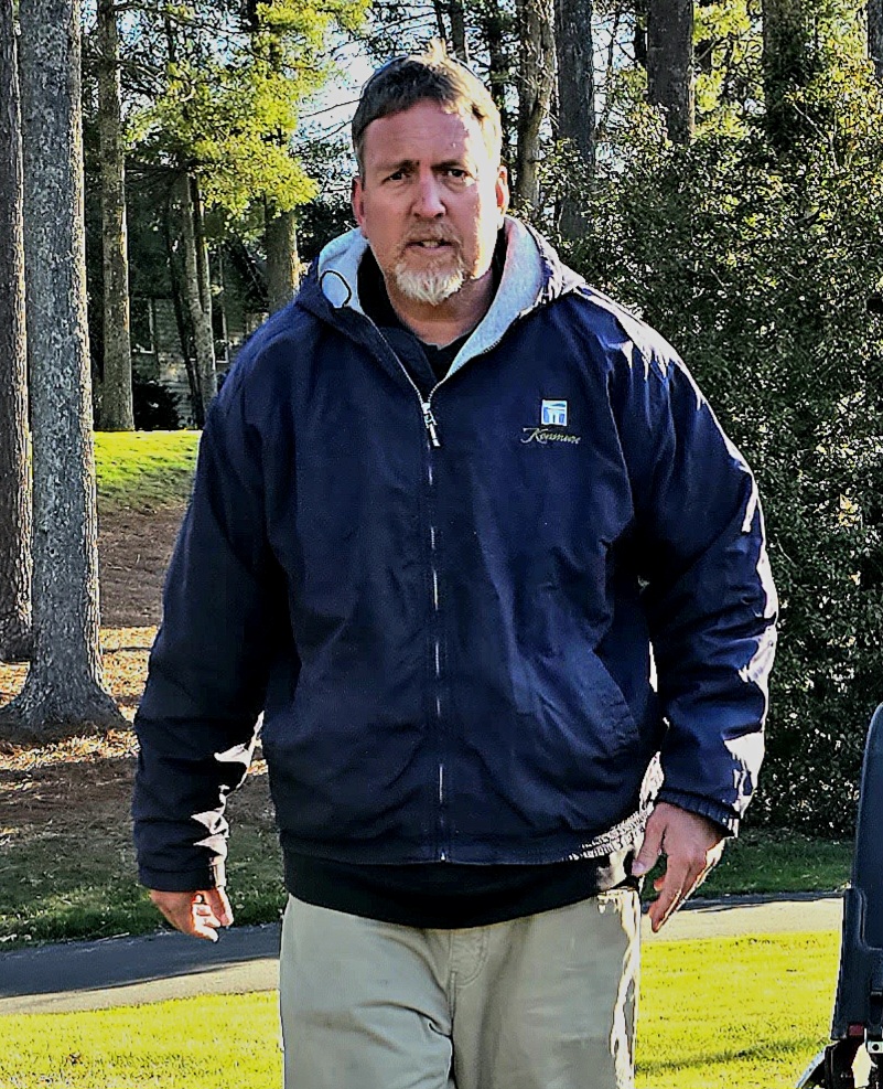 Josh standing on a putting green with maintenance equipment nearby